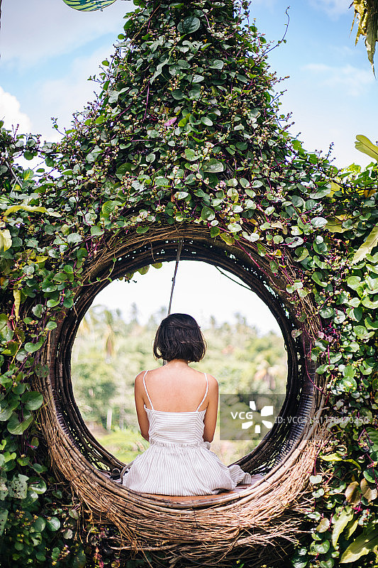 一位女游客坐在巴厘岛树上的一个大鸟巢上图片素材