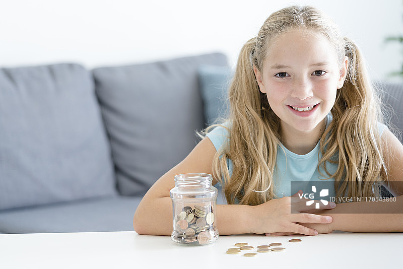 拿着储蓄罐，看着镜头微笑的八岁女孩，室内拍摄。图片素材