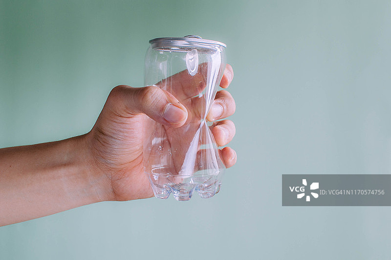 一位年轻人拿着一个绿色背景下的皱巴巴的塑料和锡制苏打水罐图片素材