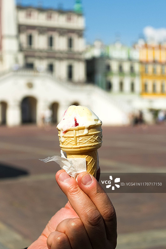 男人手持香草浆果冰淇淋甜筒，模糊的旧城背景图片素材