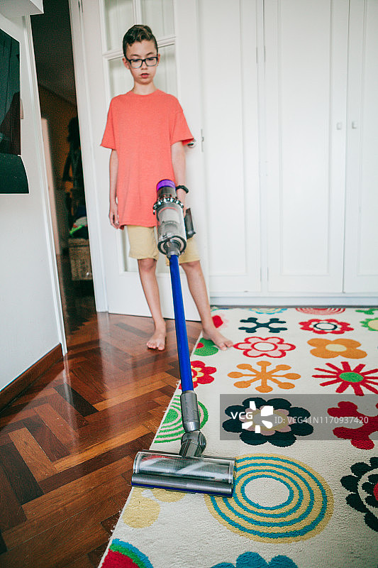 男青少年在家用地毯上使用真空吸尘器图片素材