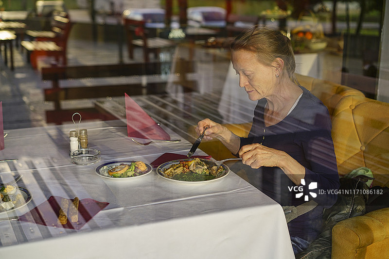 窗口倒影的妇女在餐桌上吃晚餐，塞尔维亚。图片素材