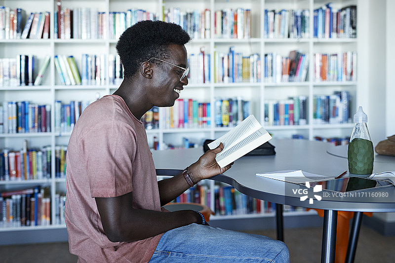 微笑的年轻人在图书馆的桌子上看书图片素材