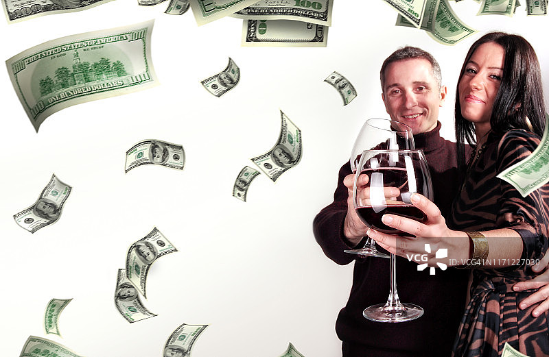 年轻情侣庆祝并在 falling money 下喝葡萄酒图片素材