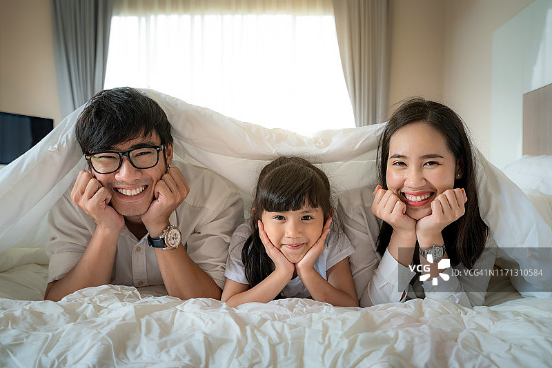 在卧室的床上度假，拥有幸福笑容的迷人亚洲年轻家庭图片素材