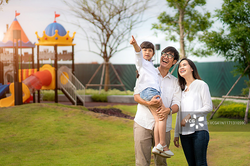 亚洲家庭在公园里散步，女儿、母亲和父亲指着什么，女儿看起来很高兴图片素材