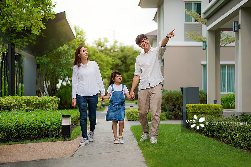 亚洲家庭在村庄新房前合影：女儿指向新家，满脸幸福图片素材
