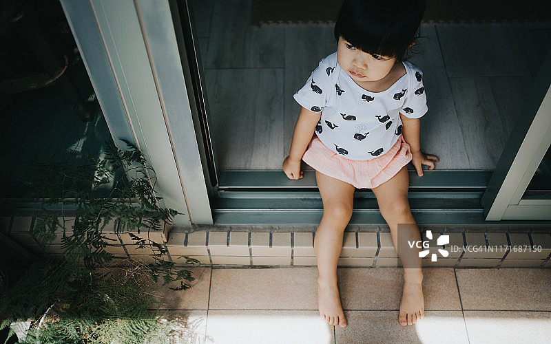 坐在阳台地板上，享受微风和阳光的可爱小女孩图片素材