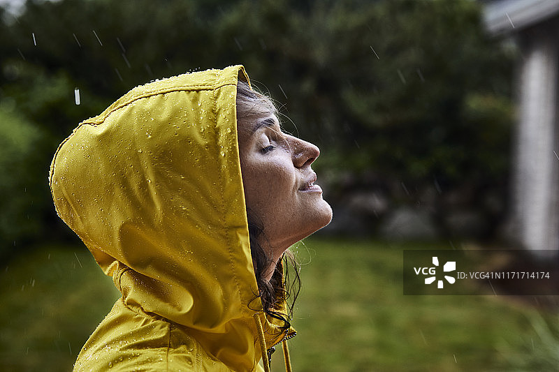 穿着雨衣的女人在花园里冒着大雨图片素材