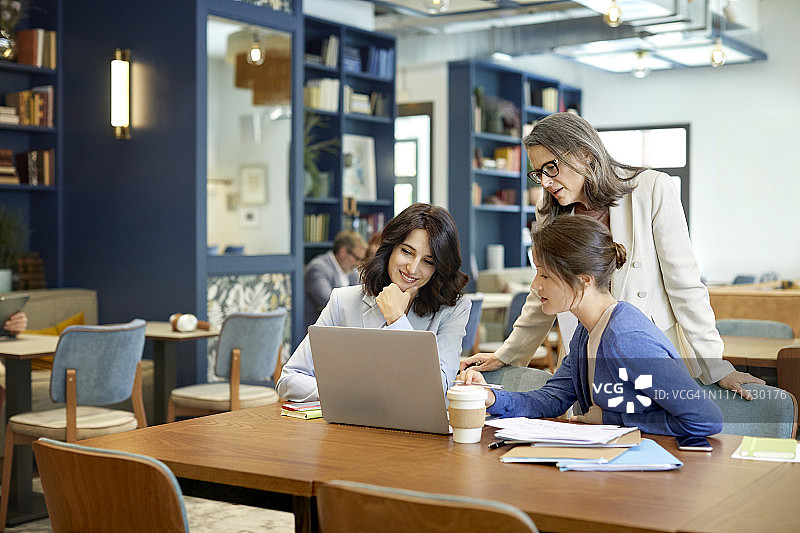 女同事在桌旁用笔记本电脑进行讨论图片素材