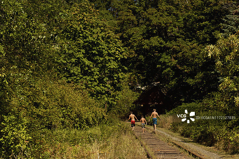 穿着泳裤的赤膊男孩走在阳光明媚的夏日铁轨上图片素材