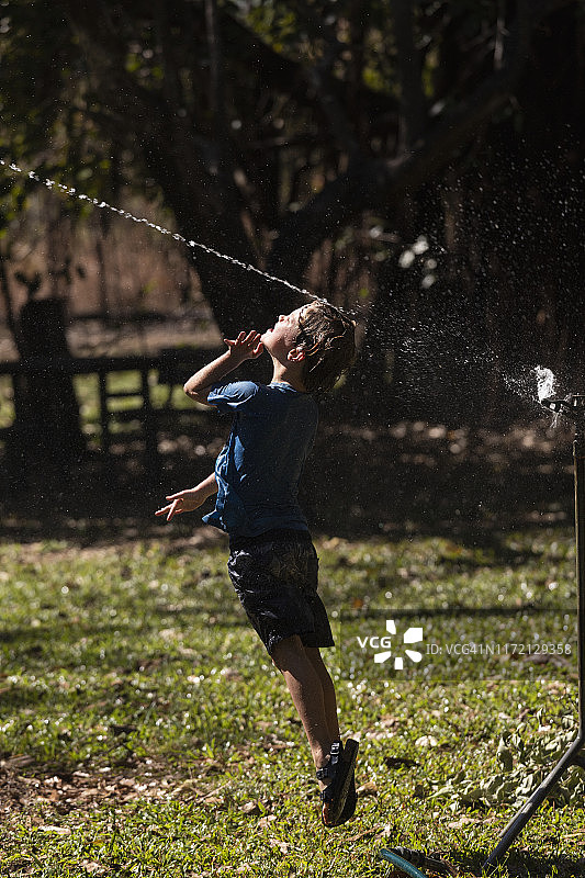 男孩在阳光明媚的后院跳入洒水器中图片素材