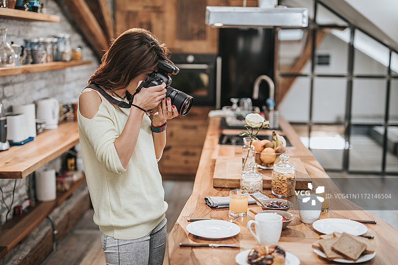 女摄影师在餐桌旁拍摄食物图片素材
