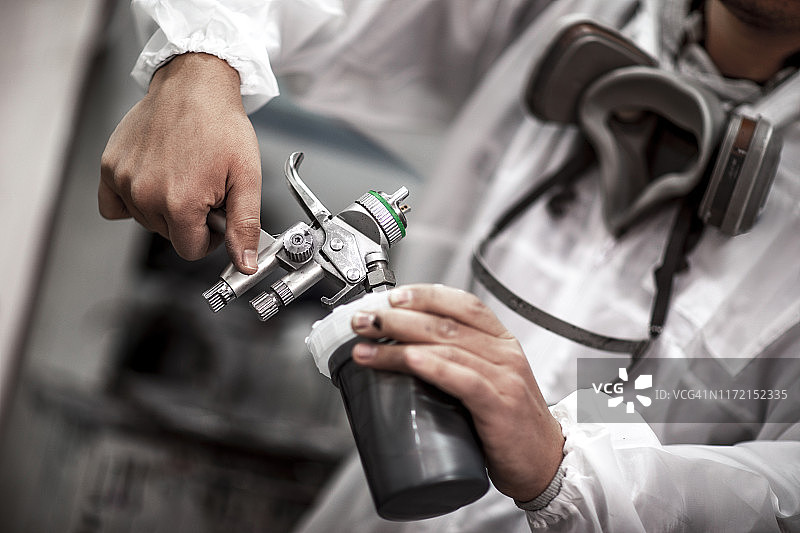 汽车喷漆工在喷漆房将油漆罐放在喷枪上图片素材