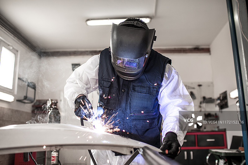 汽车修理工在车身修理店用弧焊机修理损坏的汽车零件图片素材