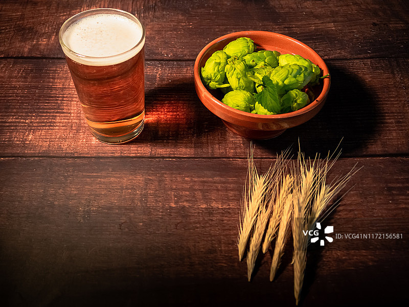 自制啤酒：一杯带有白色泡沫的淡啤酒，一个装有啤酒花、啤酒花叶和麦穗的陶碗图片素材