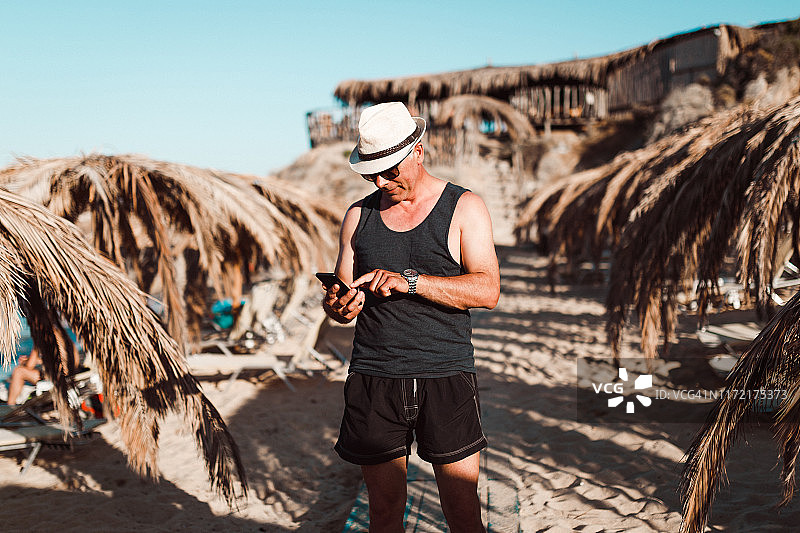 快乐的中年男人在海滩发短信图片素材