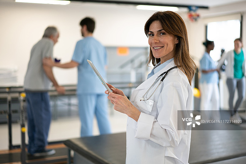 理疗康复诊所里自信的骨科医生手持平板电脑，面带微笑面向镜头图片素材