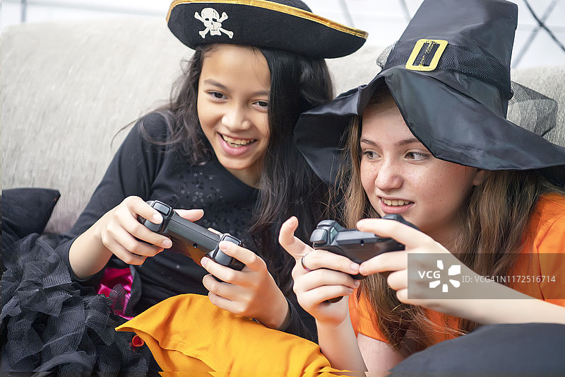 万圣节装扮的小女孩们在家里的客厅沙发上玩游戏机，欢声笑语图片素材
