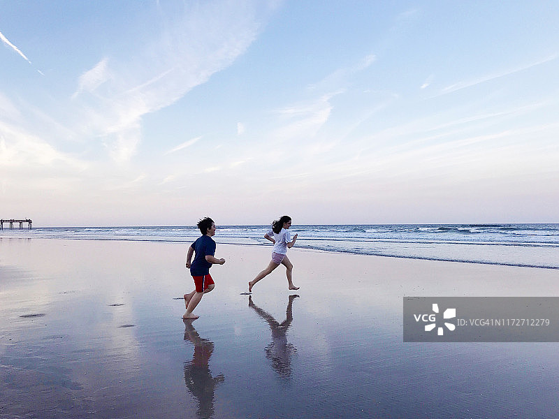 兄妹在海滩上奔跑，日落天空倒映在沙滩上图片素材