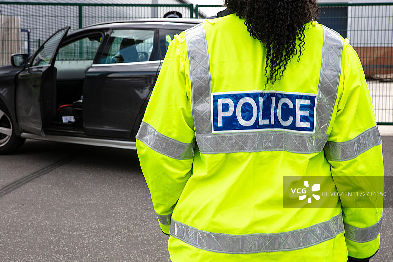 警察站在废弃车辆前，身穿高可见度警服图片素材