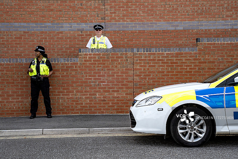两名警察在红砖大楼外站岗，警车正面照图片素材