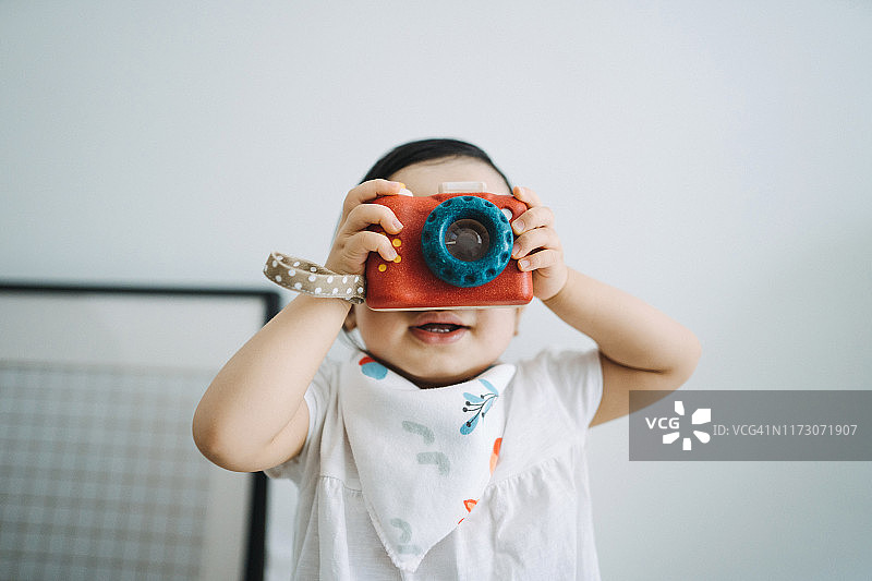 可爱的小女孩在家玩耍并用玩具相机拍照图片素材