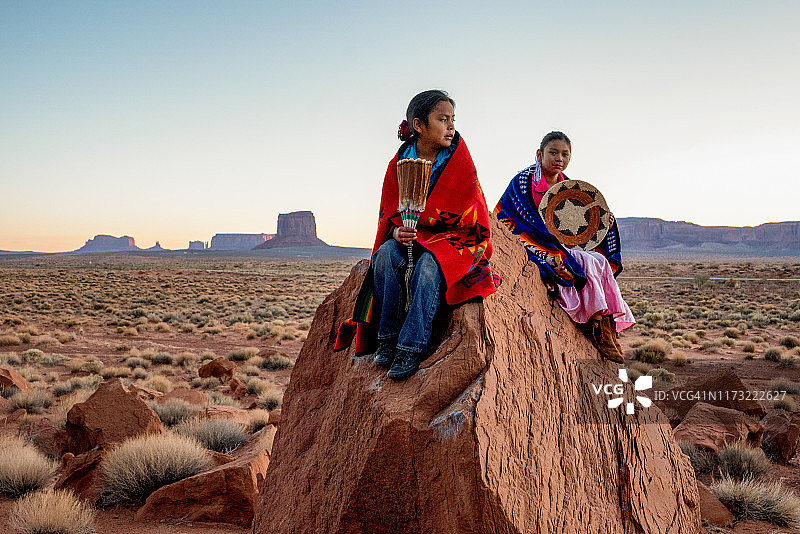 纪念碑谷中摆姿势的年轻纳瓦霍族兄妹，站在红色岩石前，背景是黎明时分沙漠中神奇的手套岩层图片素材