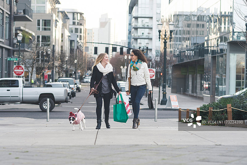 时尚年轻女性在城市街道上遛狗购物图片素材