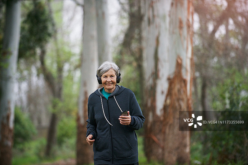老年妇女独自在森林中慢跑，听着音乐图片素材