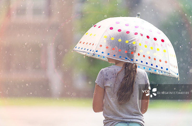 一位有着棕色长发的年轻女孩在雨中撑着波点伞的背影图片素材