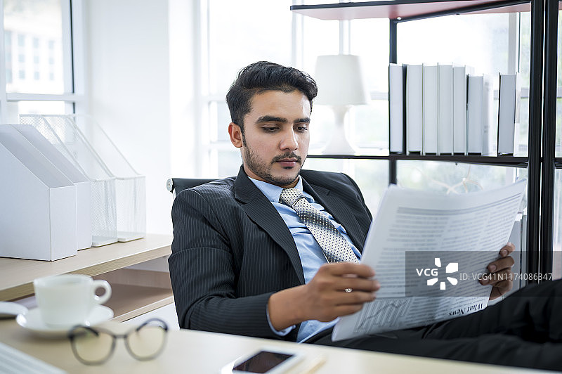 在办公室阅读报纸，面带幸福微笑的年轻商人。事业成功理念。事业目标理念。图片素材
