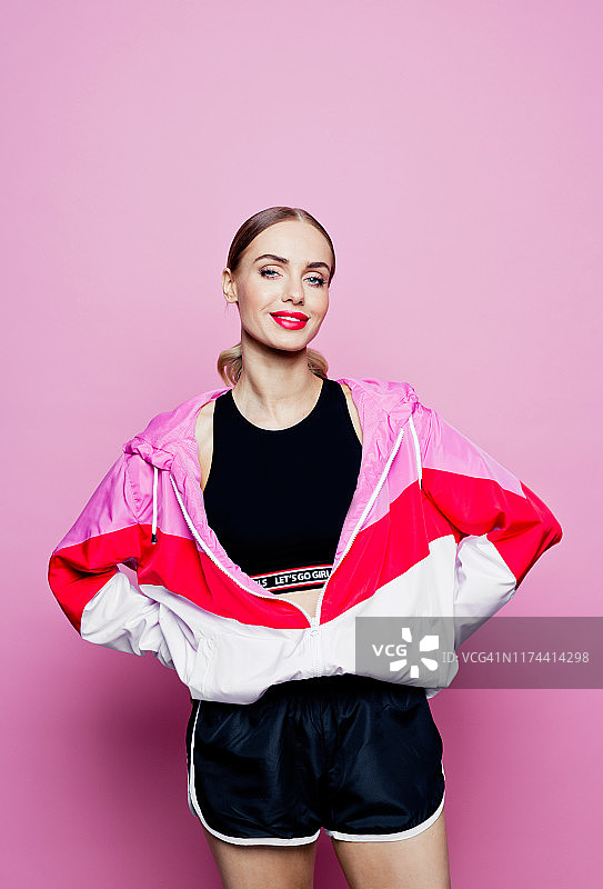 粉色背景下身穿运动服微笑女性的80年代风格肖像图片素材