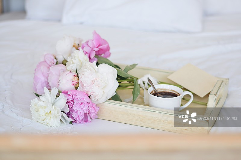 芍药花束和一杯咖啡，信封在床上托盘上图片素材