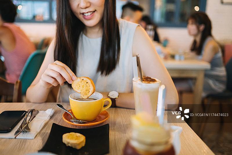 快乐的年轻女人坐在餐厅里，用面包蘸汤图片素材