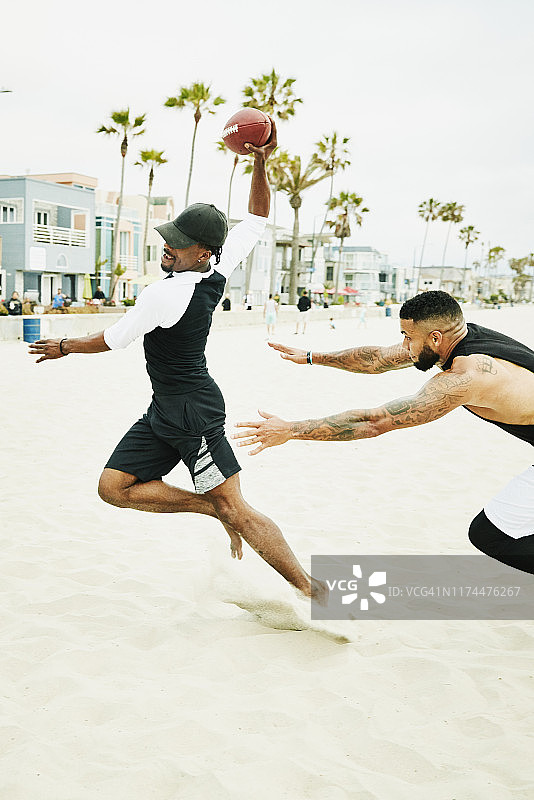 在海滩上与朋友进行足球比赛时，躲避后卫的男人图片素材