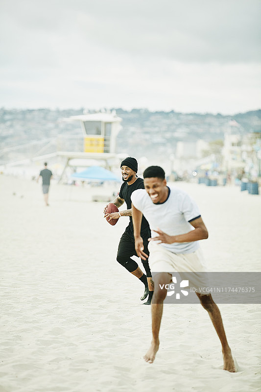 微笑的男人在海滩上与朋友们进行橄榄球比赛图片素材