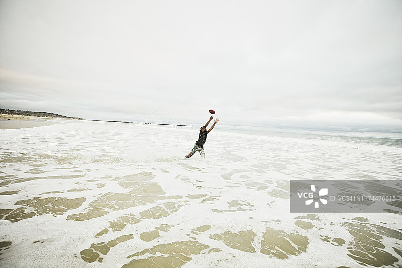 男子在海滩上跳入水中接足球图片素材