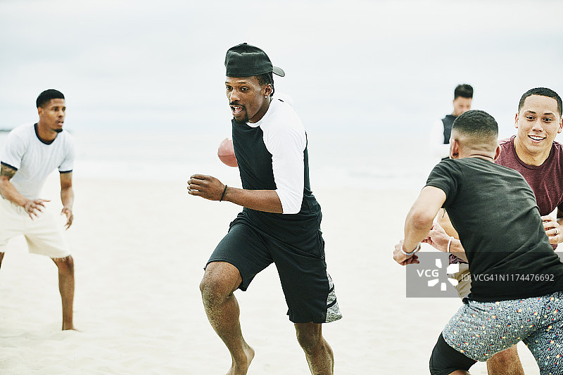 在海滩上与朋友进行腰旗橄榄球比赛时跑出去接球的男人图片素材