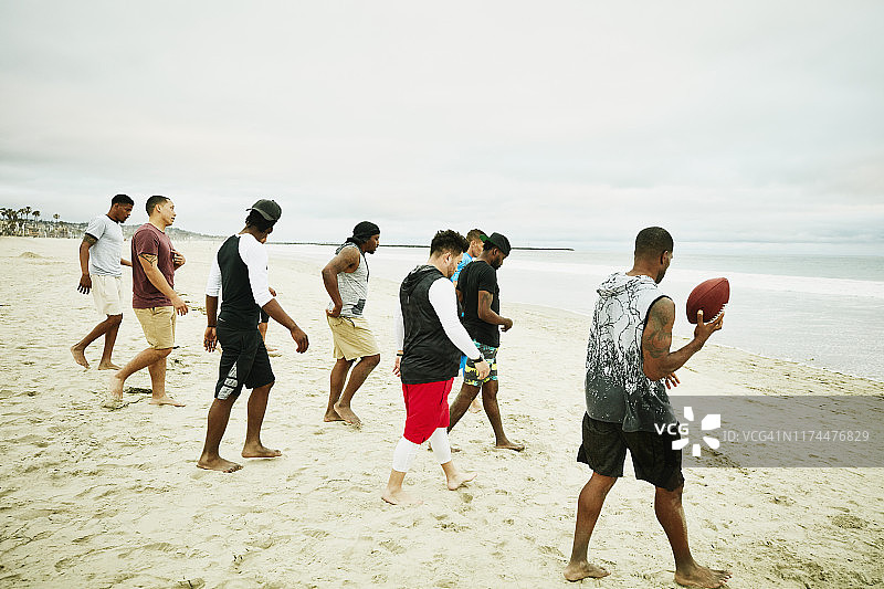朋友们在海滩玩橄榄球后走向水边图片素材