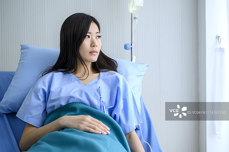 生病的亚洲年轻女性独自在医院病床上看窗外图片素材
