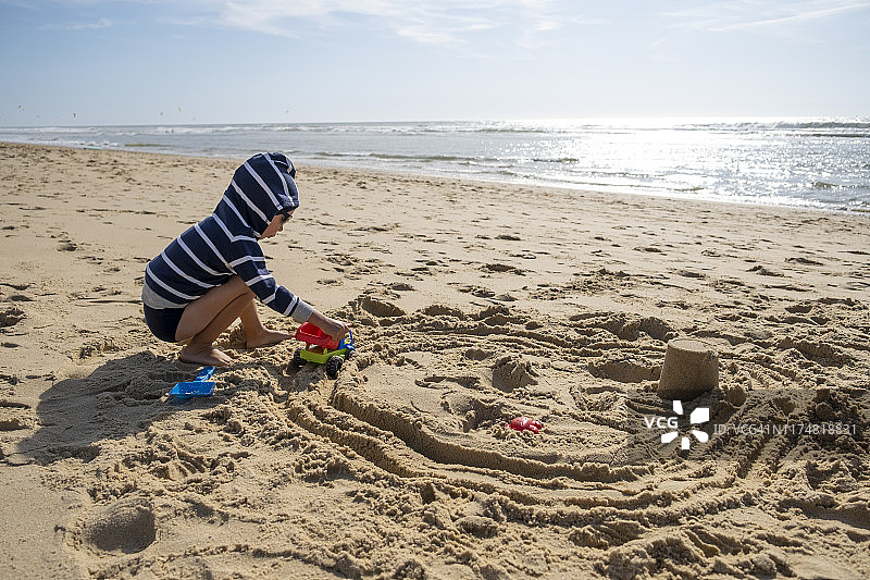 在海滩上玩卡车和堆沙堡的小男孩图片素材