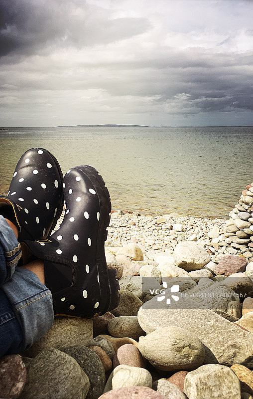 穿着圆点雨靴的女人在鹅卵石海滩上放松图片素材