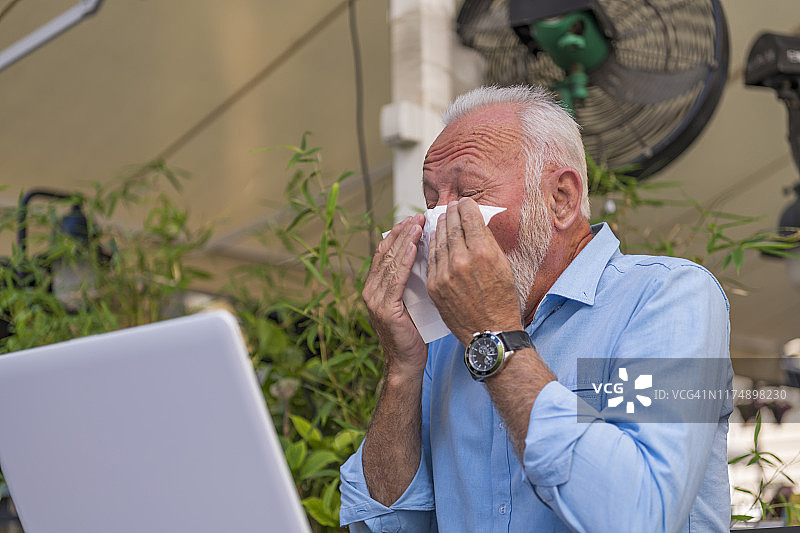 在餐厅花园里，一位年长的男人因流感在纸巾里打喷嚏图片素材