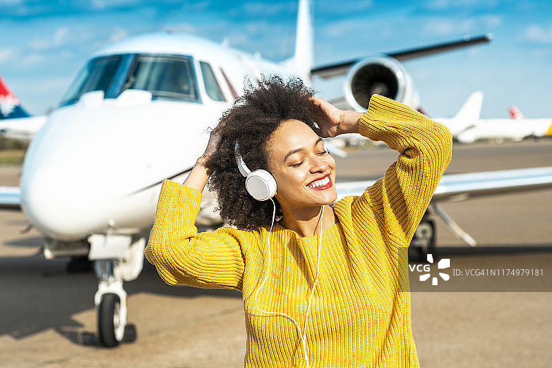 在停机坪私人飞机旁的年轻女孩戴着耳机，伴随音乐节拍跳舞图片素材