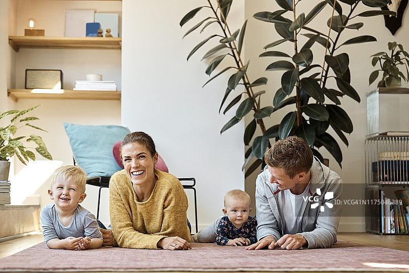 快乐的父母和孩子躺在家里的地毯上图片素材