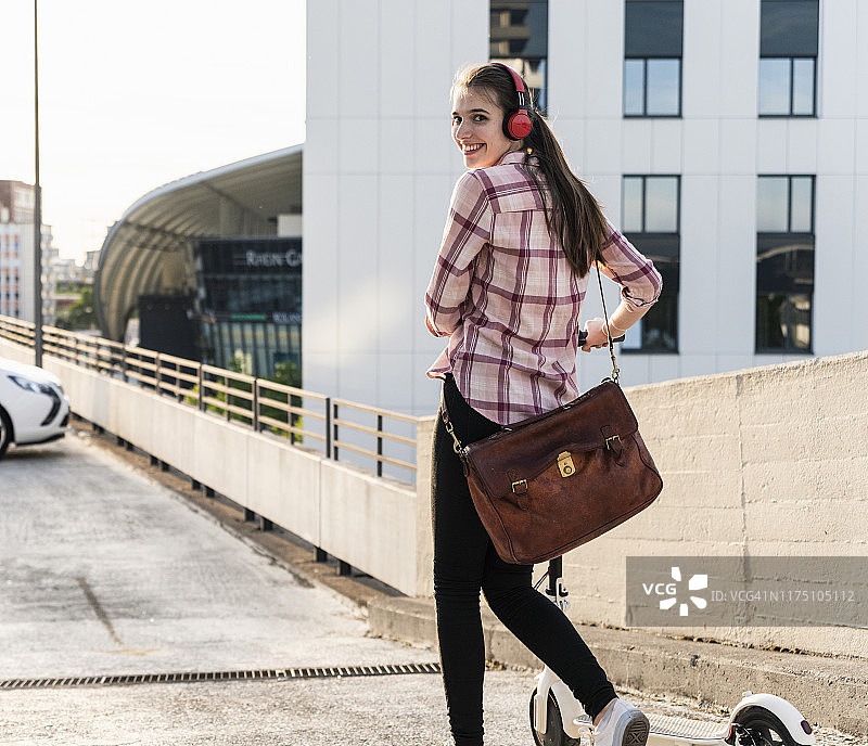 年轻女人戴耳机在停车场推动电动滑板车图片素材