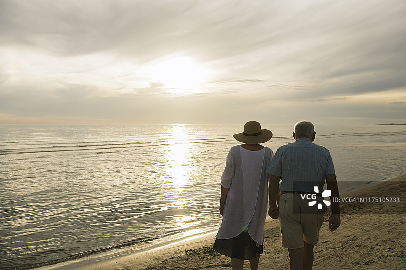 老年夫妇在拉脱维亚利耶帕亚海滩日落时手牵手散步的背影图片素材
