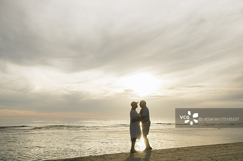 年长的夫妇在海滩上日落时分面对面站立，拉脱维亚图片素材