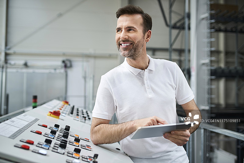 在工厂控制面板前使用平板电脑的微笑男人图片素材